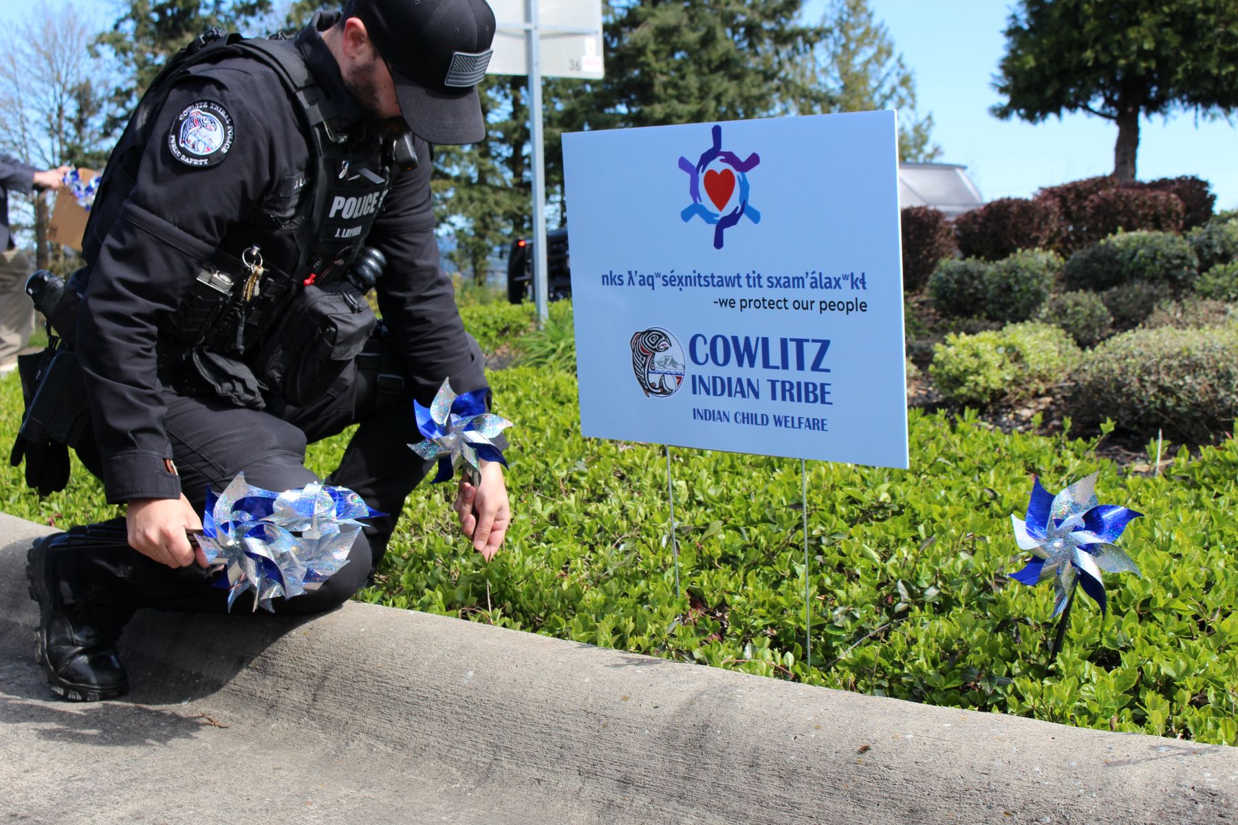 Cowlitz Tribal Public Safety Officer placing Blue Ribbon Pin Wheels in the ground on the Cowlitz Reservation in Ridgefield near a sign that states  nks ƛʼaqʷséx̣nitstawt tit sxamʼálaxʷkɬ — "We protect our people"