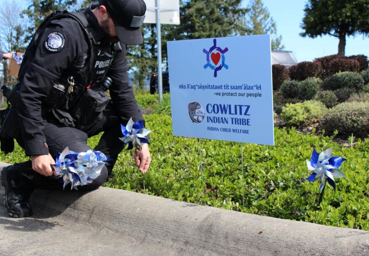 Cowlitz Tribal Public Safety Officer placing Blue Ribbon Pin Wheels in the ground on the Cowlitz Reservation in Ridgefield near a sign that states  nks ƛʼaqʷséx̣nitstawt tit sxamʼálaxʷkɬ — "We protect our people"